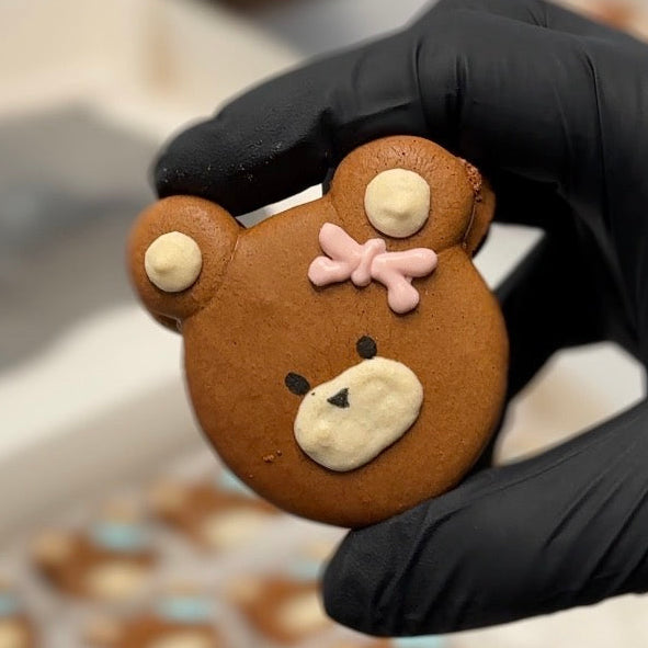 Hand holding a teddy bear-shaped macaron with a pink bow